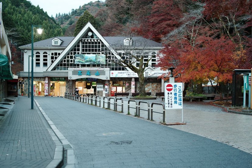 紅葉が美しい秋の高尾山ケーブルカー清滝駅の正面を撮影した画像で、三角屋根の駅舎と左右に並ぶ樹木が印象的に写っています。